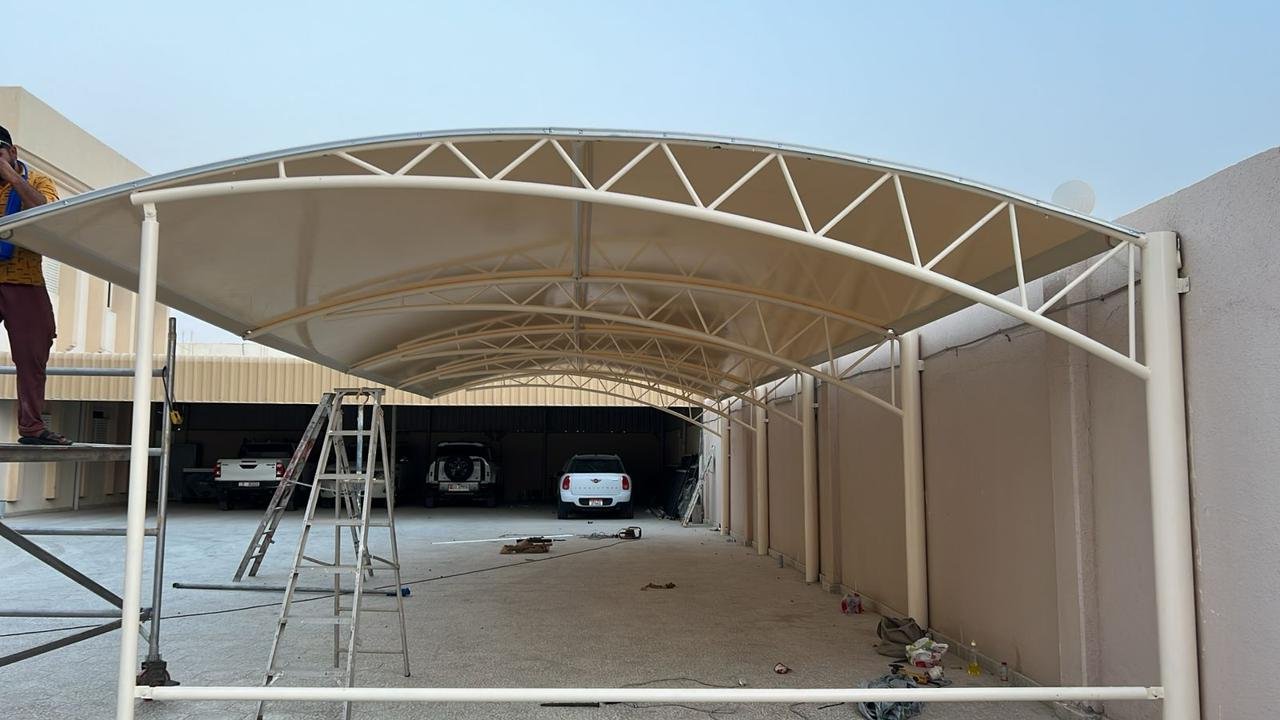 Large tensile fabric car parking shade with arched canopy and white steel frame under installation at a private villa in Abu Dhabi
