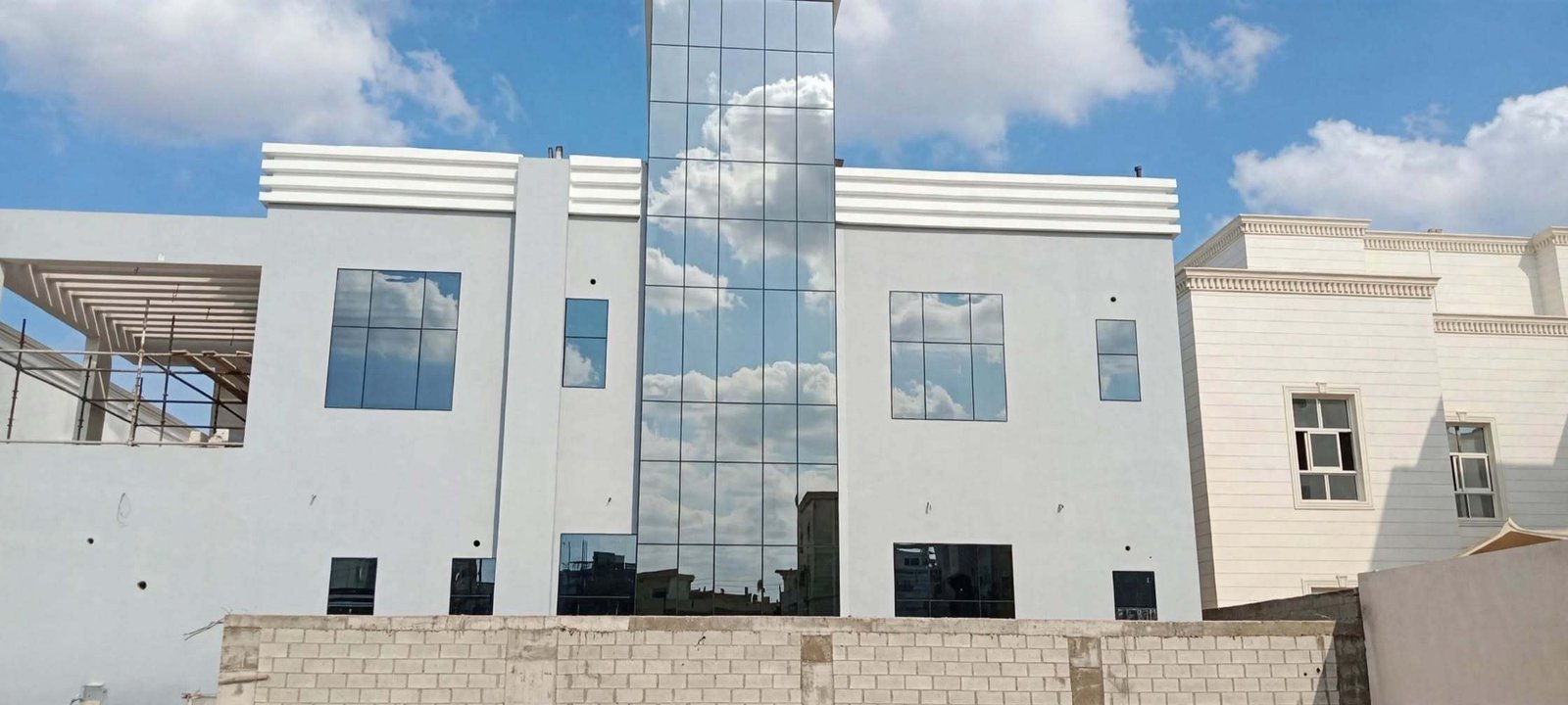 Villa facade under construction with scaffolding, showing vertical aluminium framing being installed in Abu Dhabi