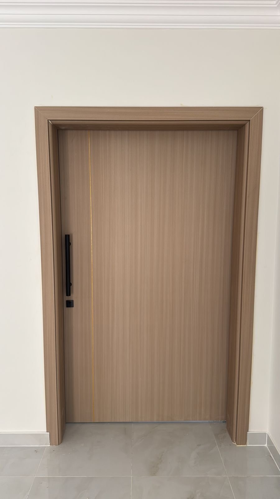 Modern WPC door with light wood-grain texture, gold inlay line and long black handle, installed in a villa interior in Abu Dhabi by A R Aluminium and Glass